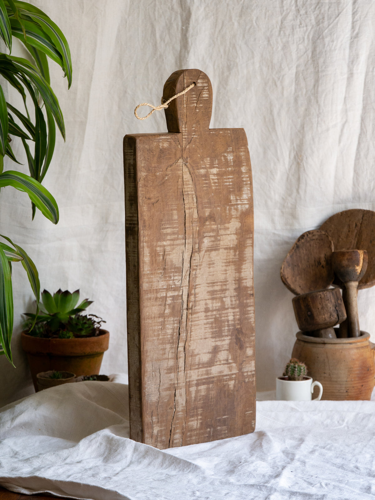A large vintage wooden chopping board from south west France, shaped by years of use and hand-worn edges. Its rough texture and deep patina tell the story of daily bread, shared meals, and time well lived.