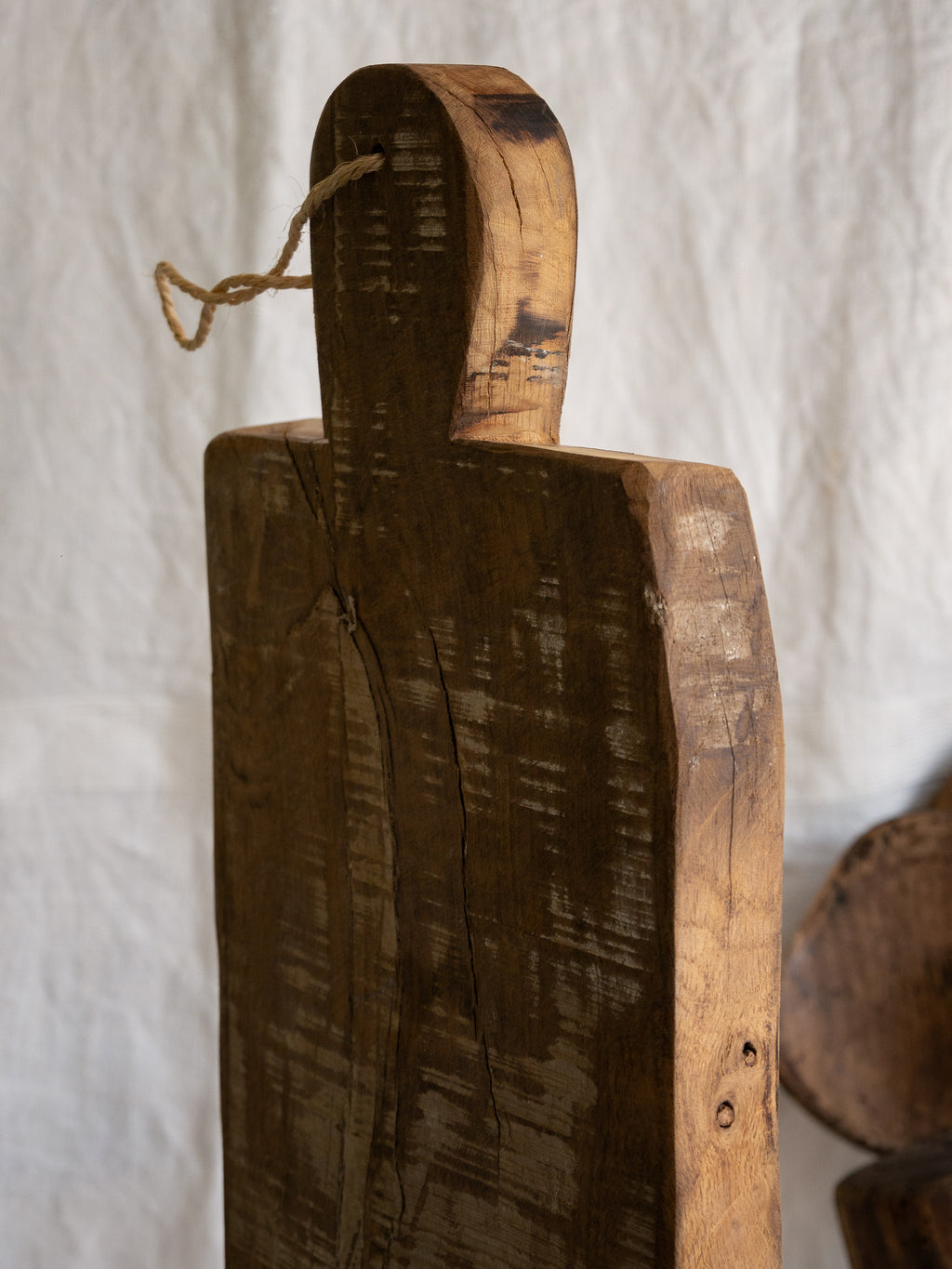 A large vintage wooden chopping board from south west France, shaped by years of use and hand-worn edges. Its rough texture and deep patina tell the story of daily bread, shared meals, and time well lived.