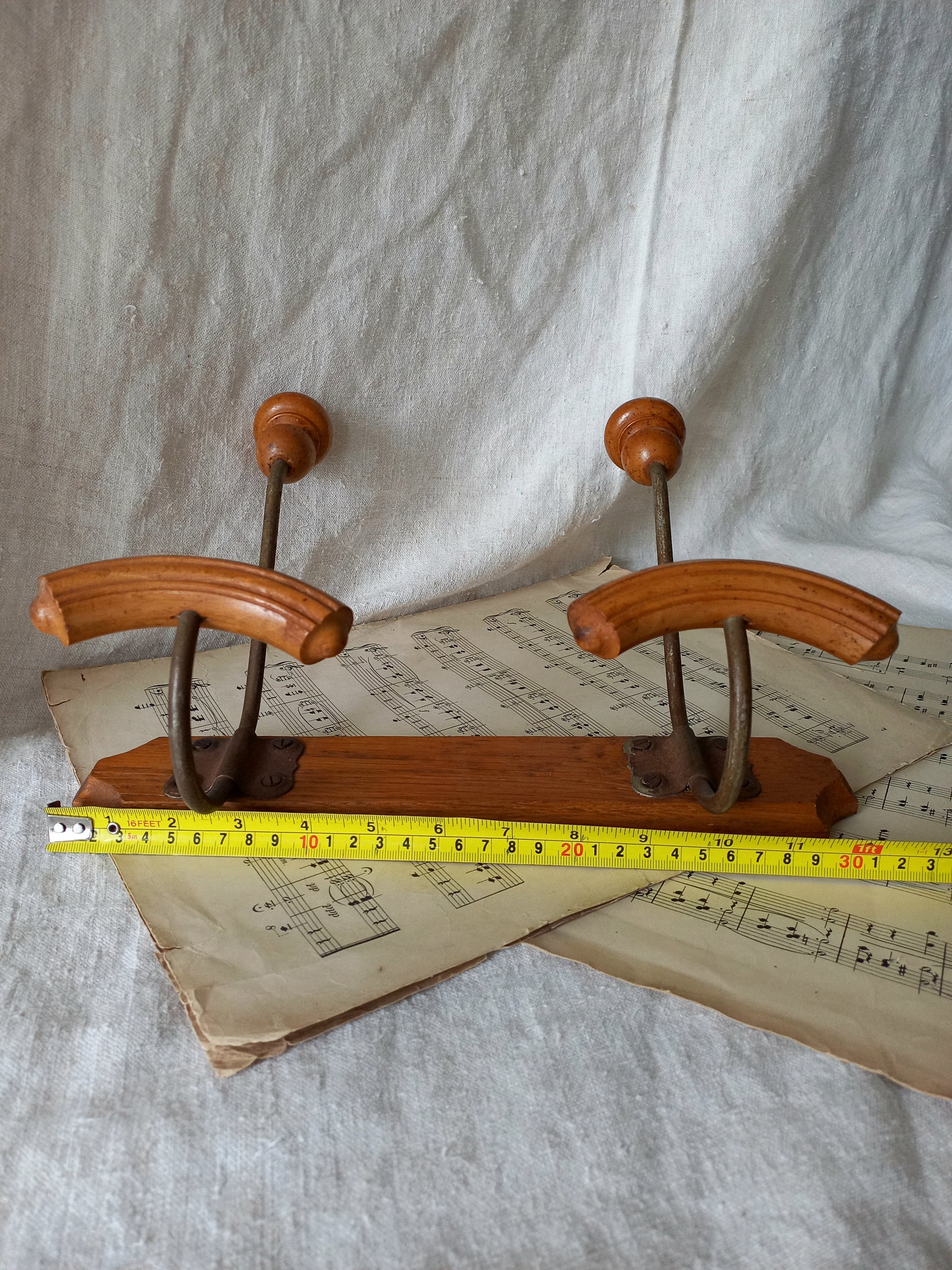 Wooden coat rack with metal hooks on a sheet of music, measured against a tape measure.