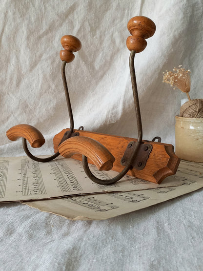 Wooden and metal coat and hat rack on a textured surface with a vase and dried plants in the background