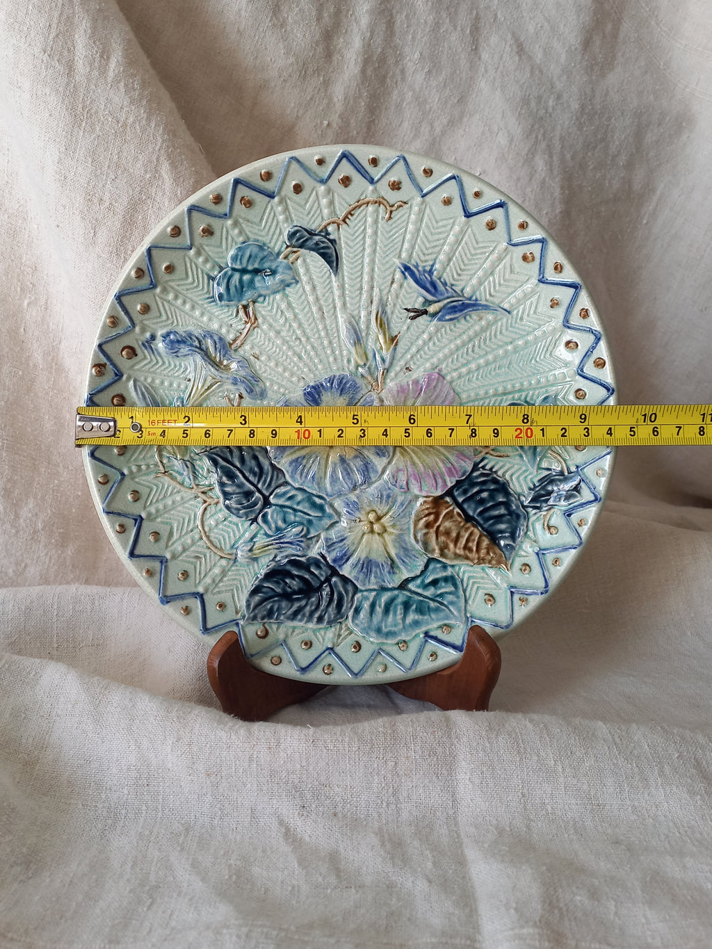 Antique Wasmuel blue floral majolica plate with designs in relief with yellow tape measure for reference.