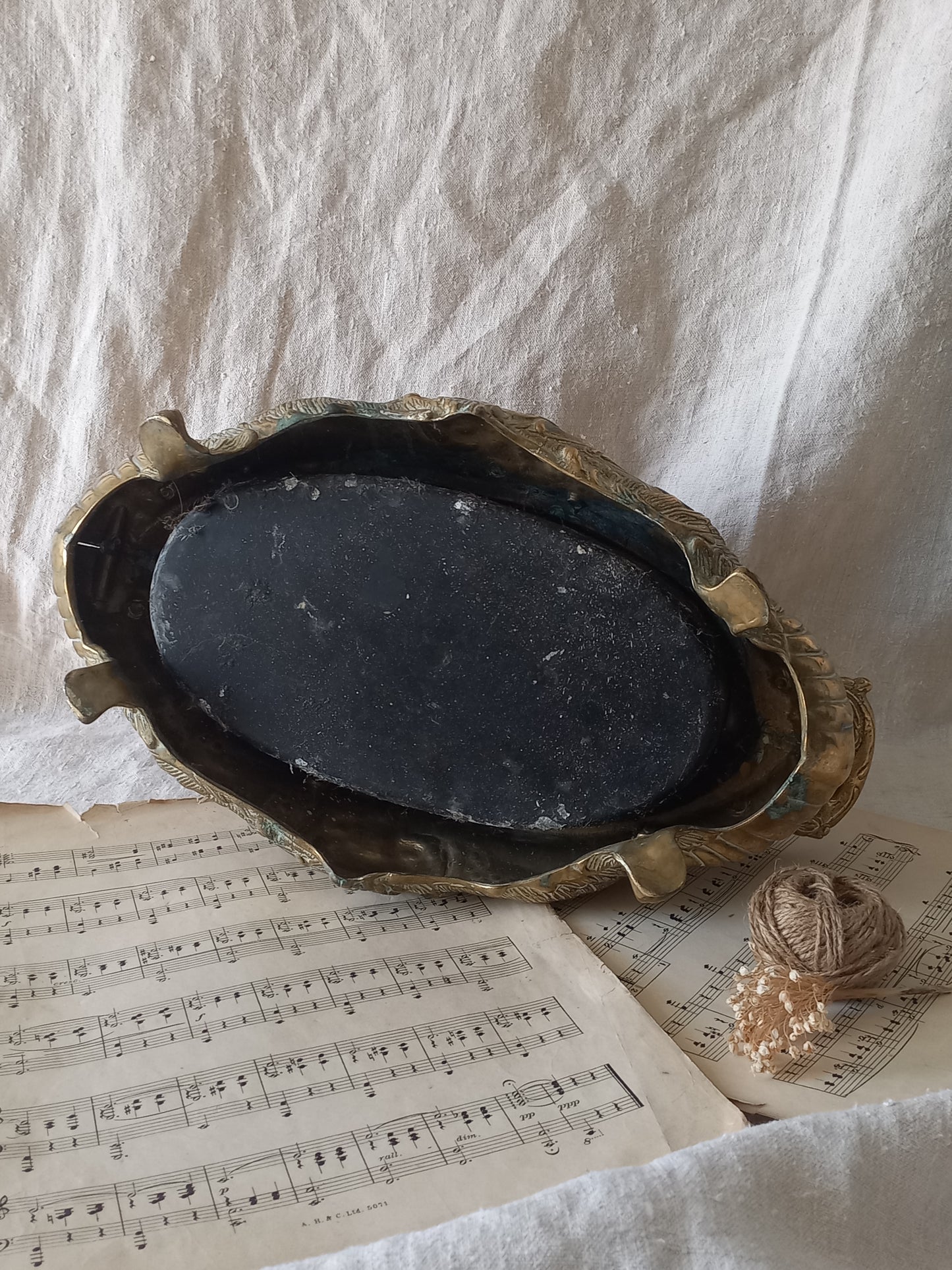 Close-up of an ornate antique decorative planter resting on a vintage sheet music page against a draped white fabric background.