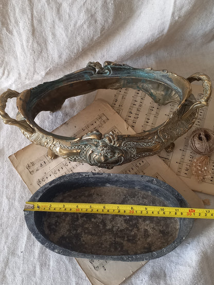 An ornate antique decorative planter resting on a vintage sheet music page against a draped white fabric background with a tape measure for reference.