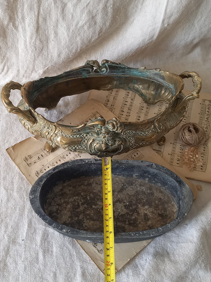 An ornate antique decorative planter resting on a vintage sheet music page against a draped white fabric background with a tape measure for reference.