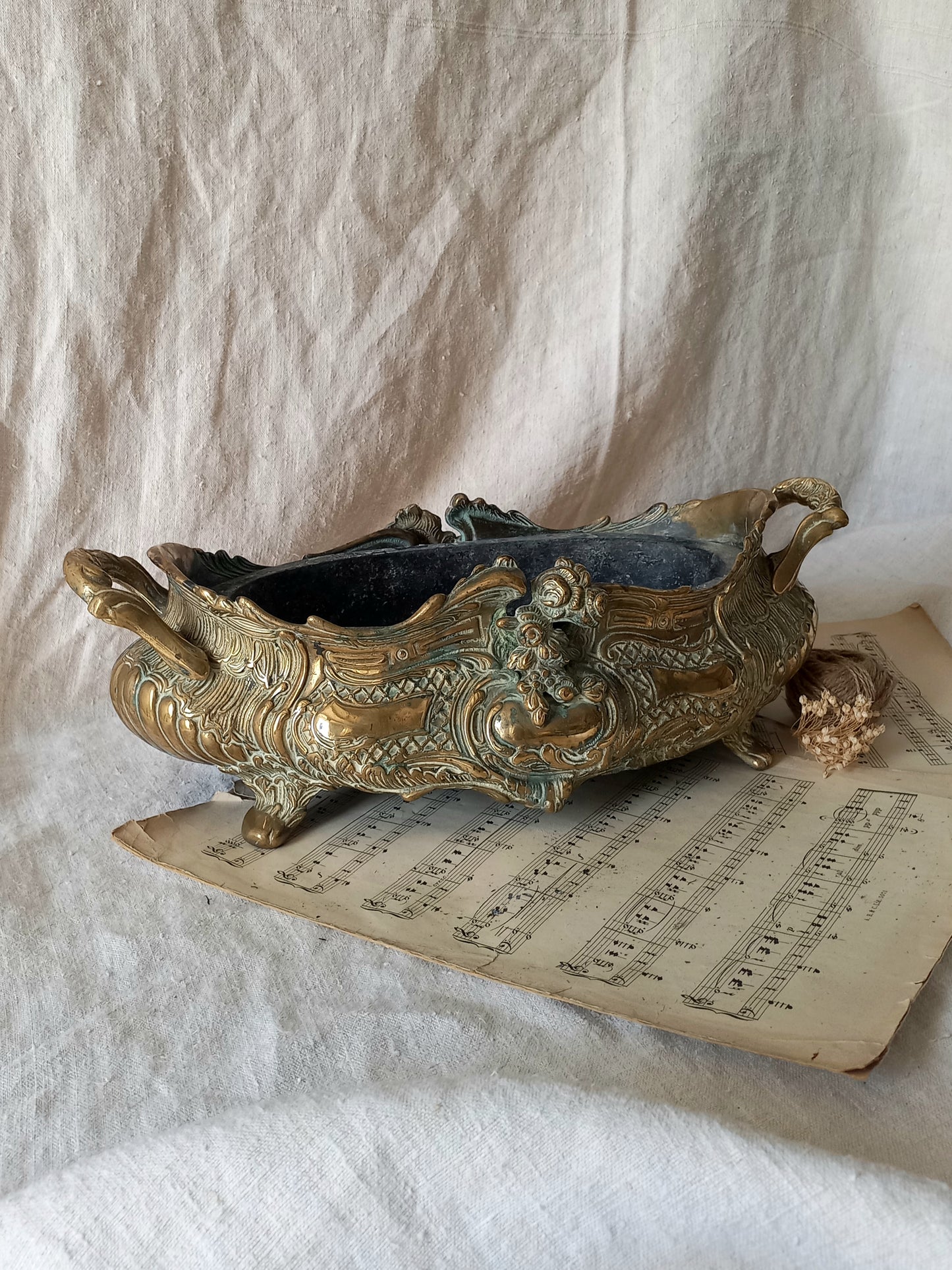 An ornate antique decorative planter resting on a vintage sheet music page against a draped white fabric background.