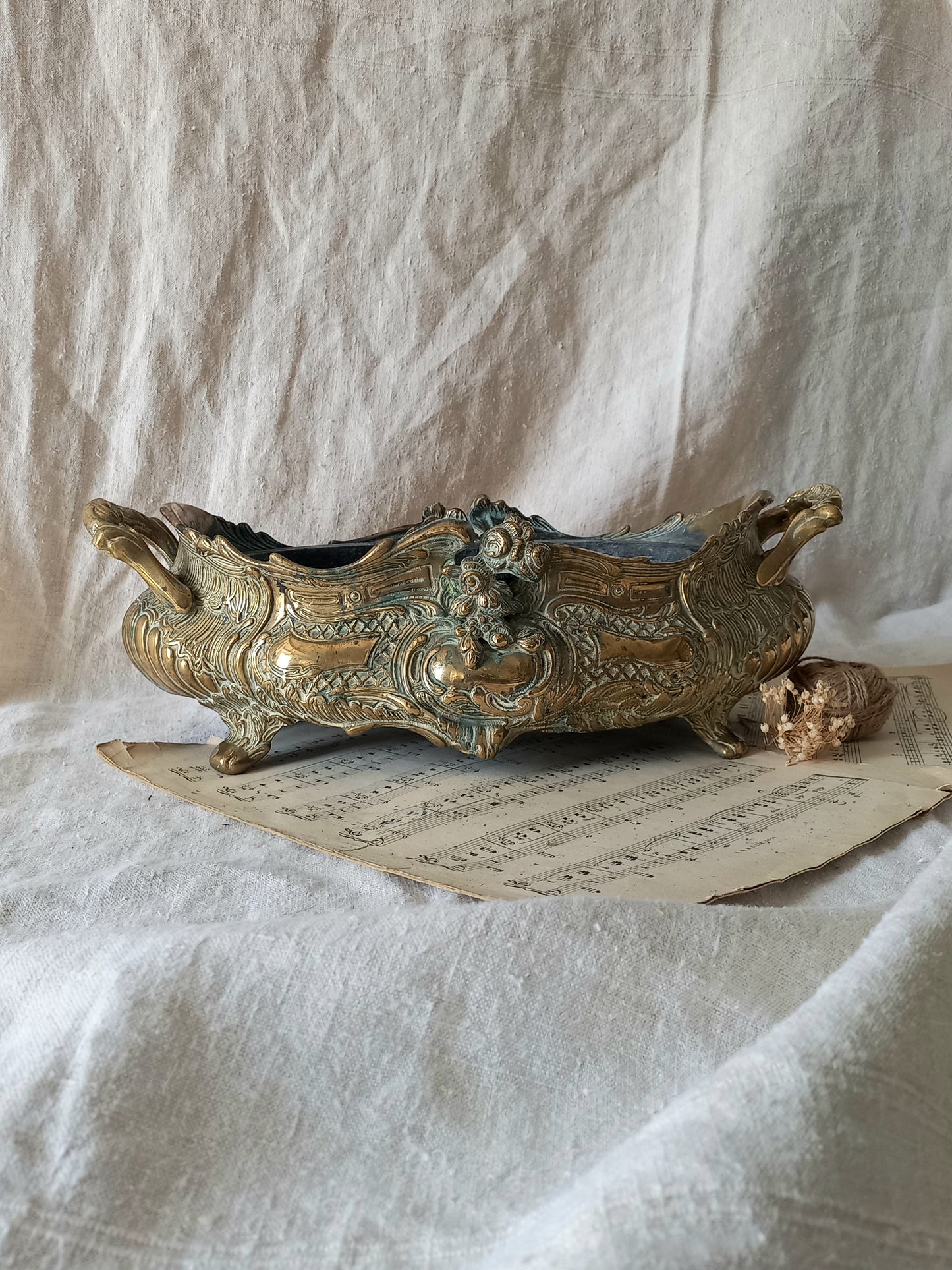 An ornate antique decorative planter resting on a vintage sheet music page against a draped white fabric background.