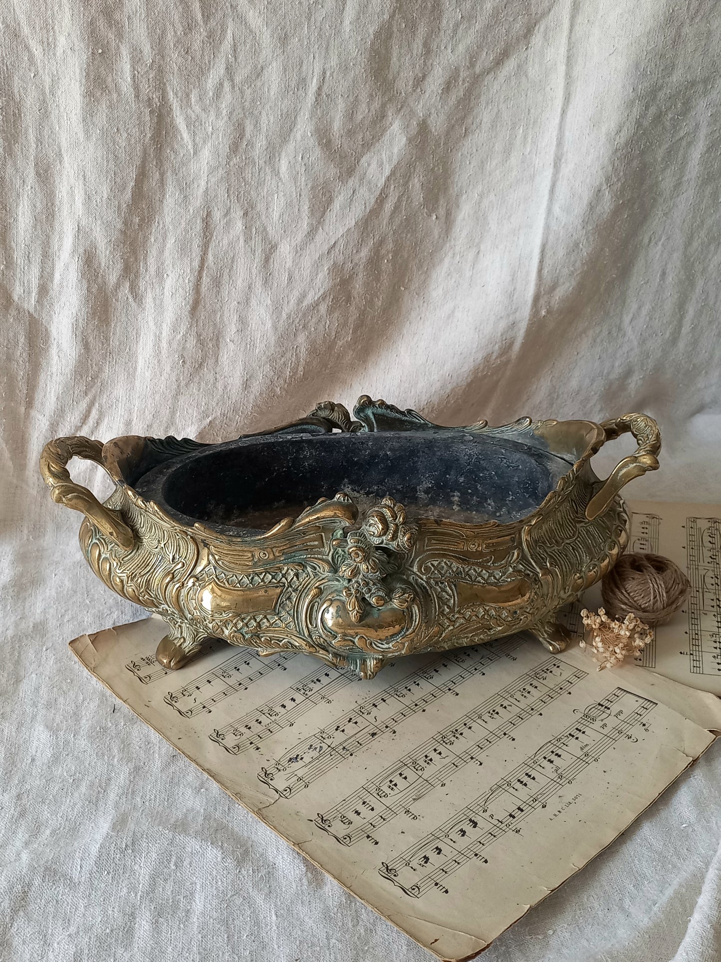 An ornate antique decorative planter resting on a vintage sheet music page against a draped white fabric background.