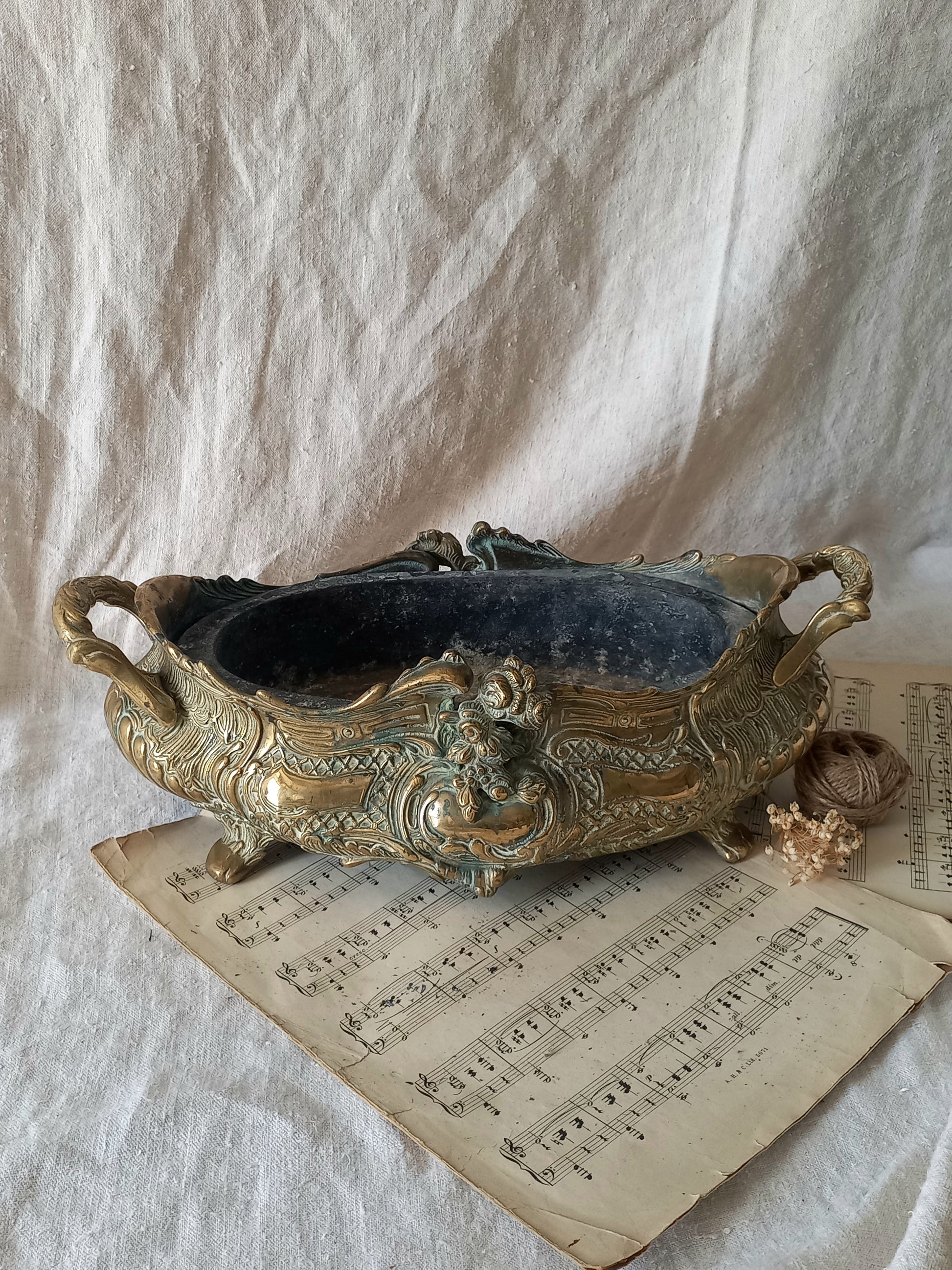 An ornate antique decorative planter resting on a vintage sheet music page against a draped white fabric background.