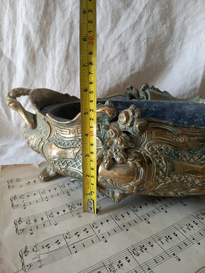 An ornate antique decorative planter resting on a vintage sheet music page against a draped white fabric background with a tape measure for reference.
