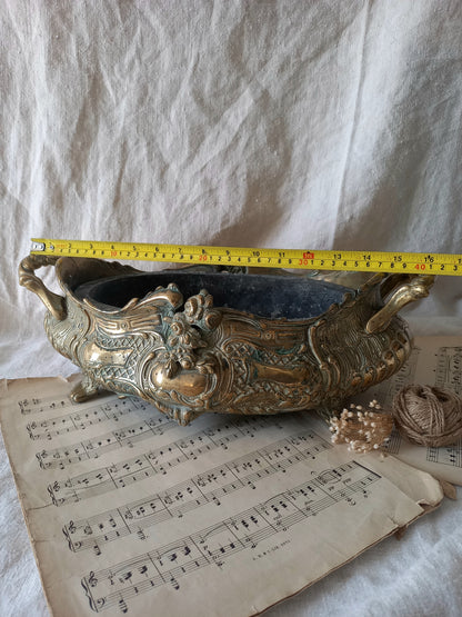 An ornate antique decorative planter resting on a vintage sheet music page against a draped white fabric background with a tape measure for reference.