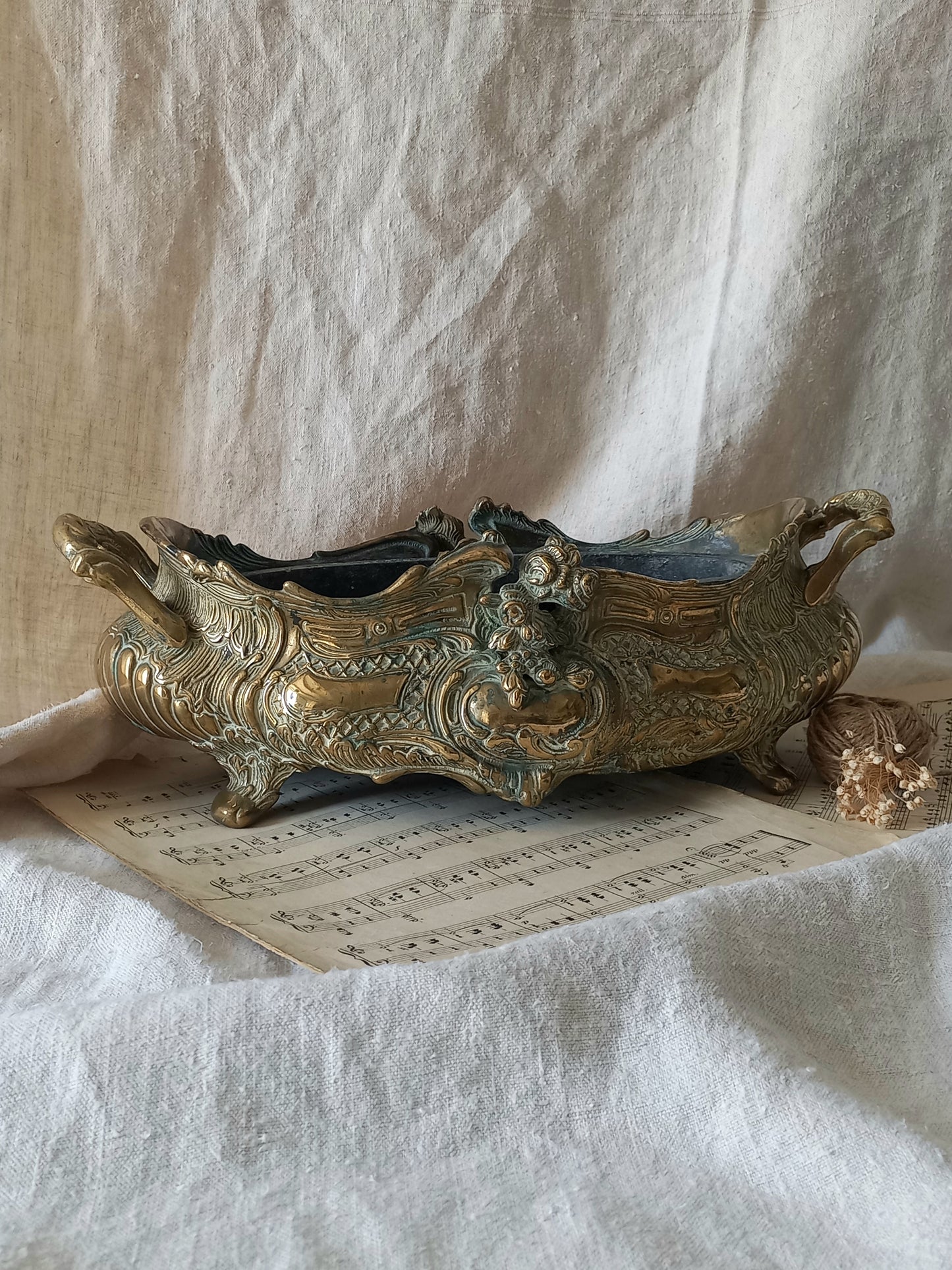 An ornate antique decorative planter resting on a vintage sheet music page against a draped white fabric background.