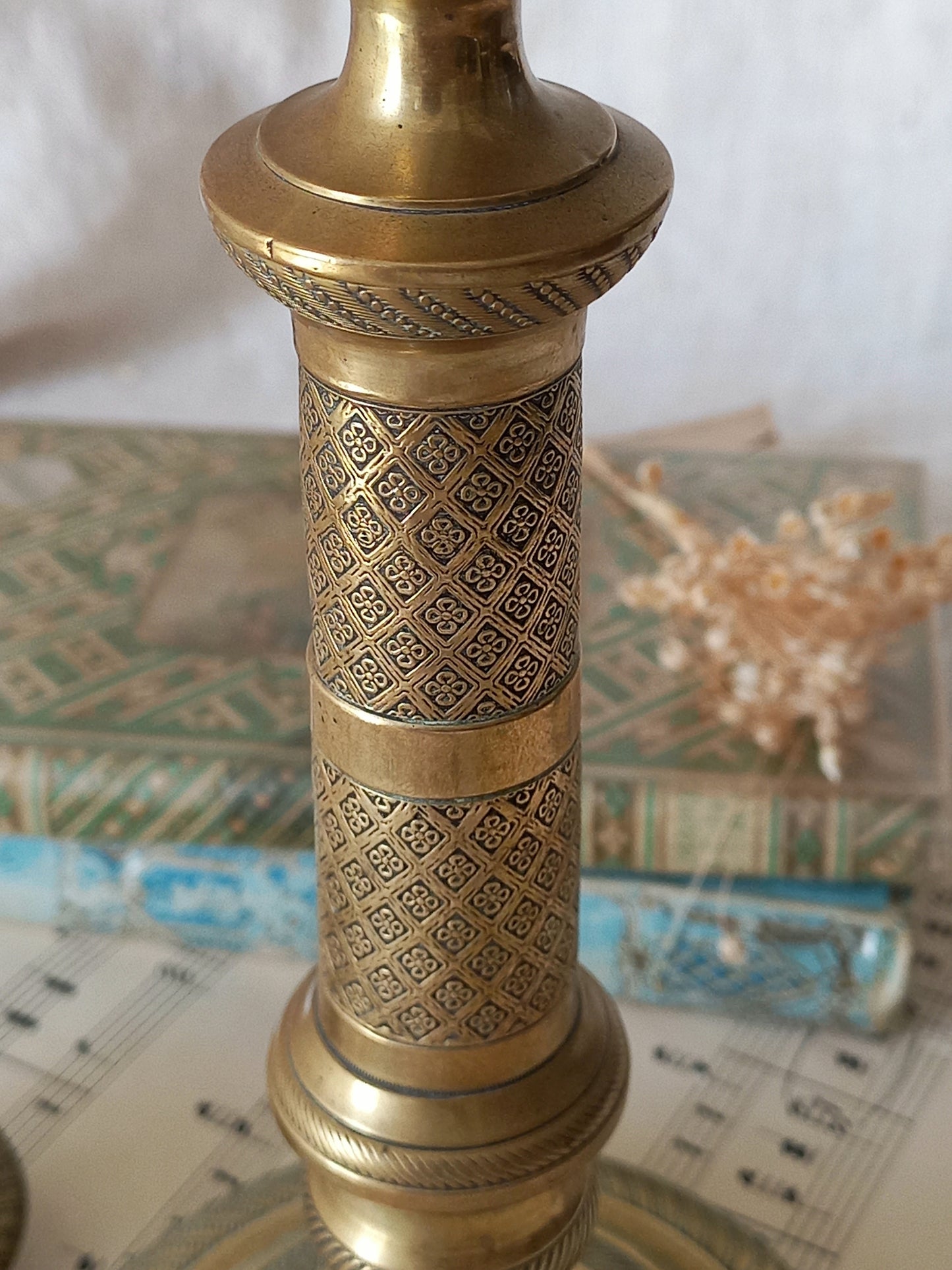 An ornate brass candle holder with intricate geometric patterns, shown in a close-up shot with vintage books and sheet music in the background.