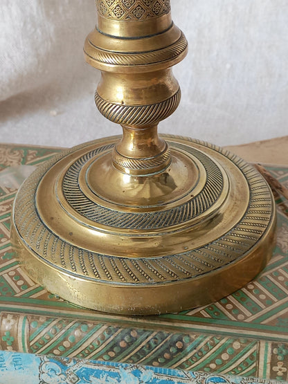 Close-up of a brass candle holder base with intricate engraved patterns, resting on a decorative green and gold patterned surface.