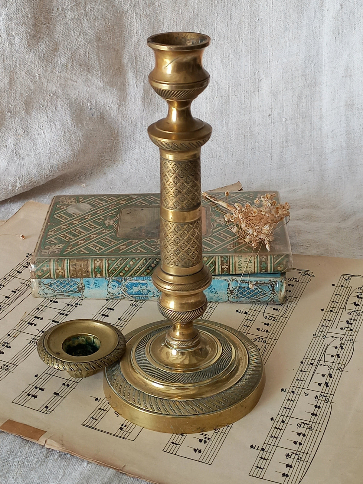 An antique brass candlestick holder with its matching lid placed beside it, styled on a sheet of musical sheet music with an old book in the background.