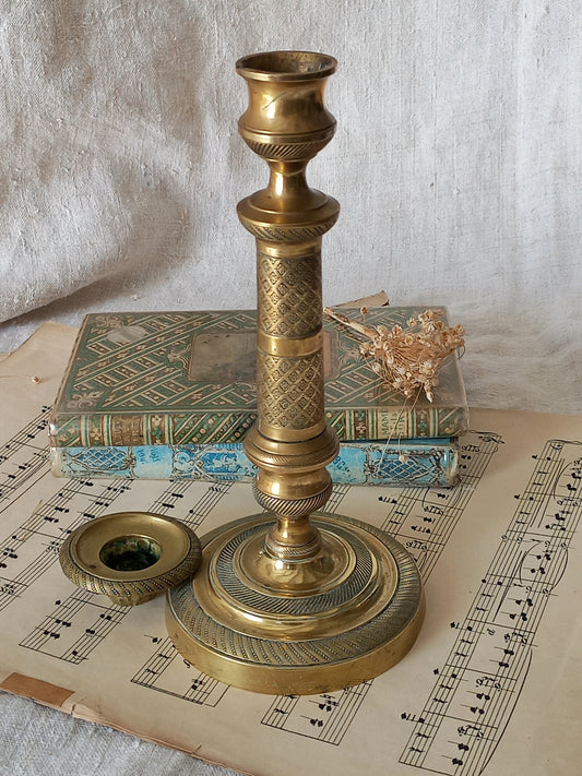 An antique brass candlestick holder with its matching lid placed beside it, styled on a sheet of musical sheet music with an old book in the background.