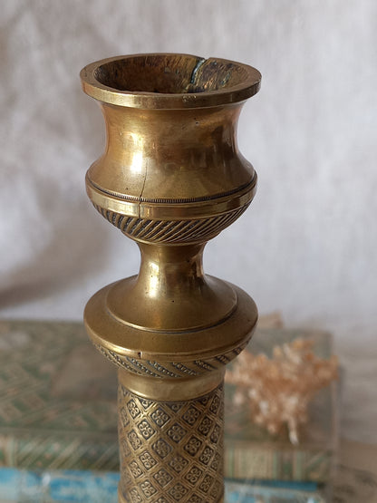 Close-up of a brass candle holder with engraved patterns and a flared opening, shown against a soft light background.