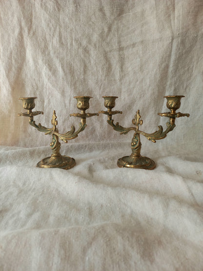 A pair of ornate brass candelabras displayed on a draped white fabric background.