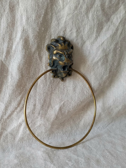 An antique brass lion head ring holder with a circular pull, resting on a textured off-white fabric background.