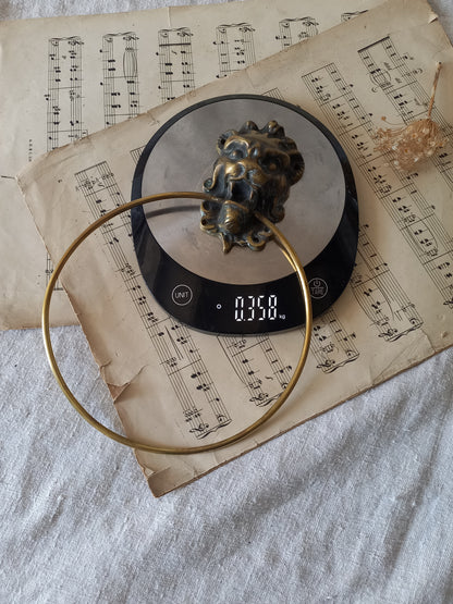 Vintage brass towel ring holder with a lion head sculpted on the front, displayed on top of an antique sheet music page and digital scales for reference.