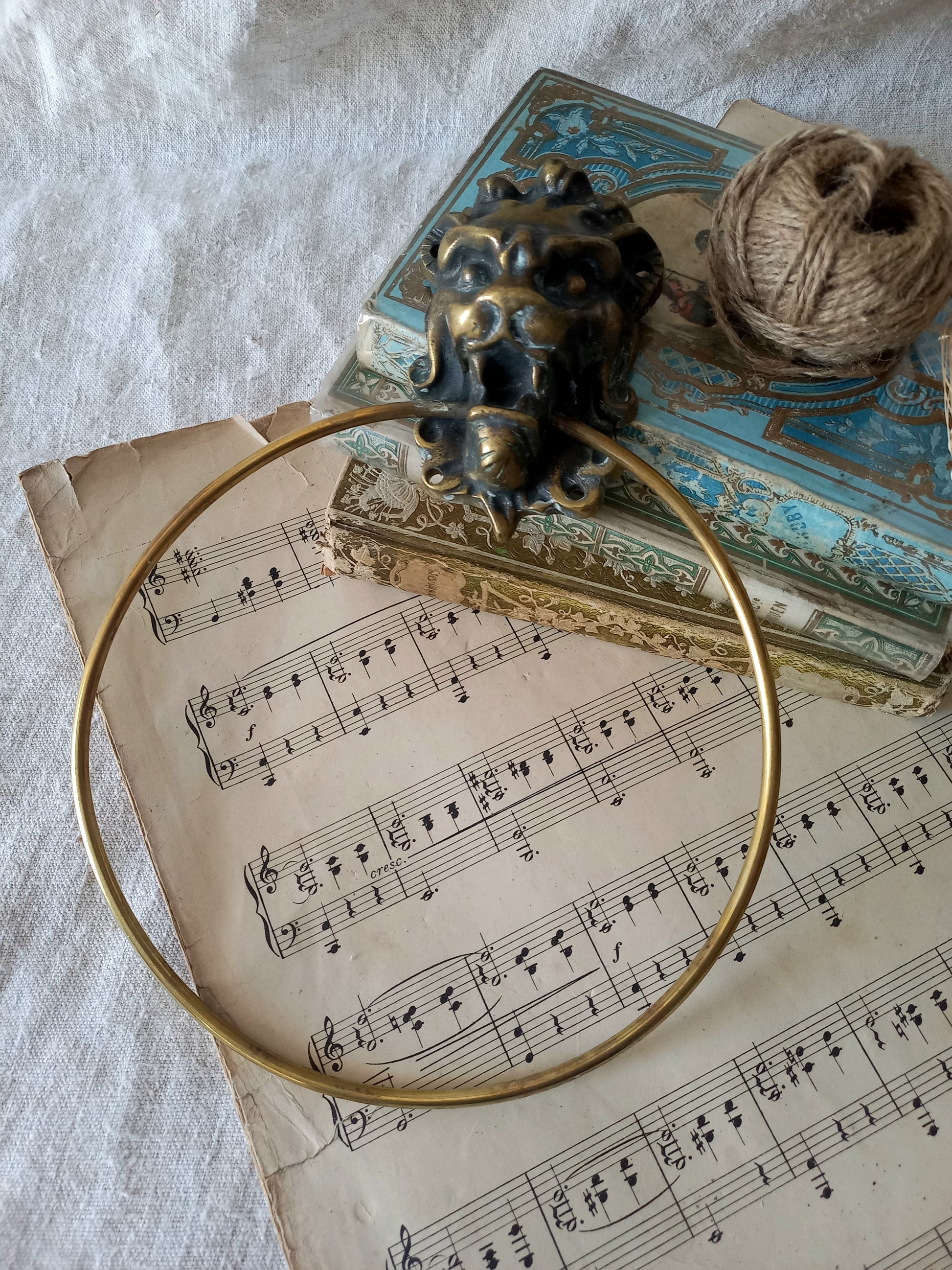 vintage brass towel ring holder with a lion head sculpted on the front, displayed on top of an antique sheet music page with decorative books and a ball of twine in the background.