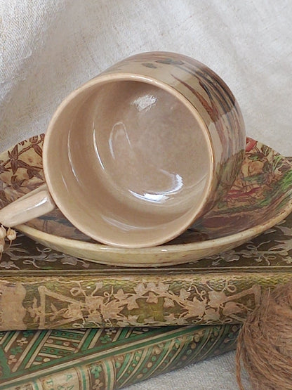 A little antique cup and saucer with oriental influenced design depicting ducks, butterflies, flowers and bamboo shoots, placed on an antique books display.
