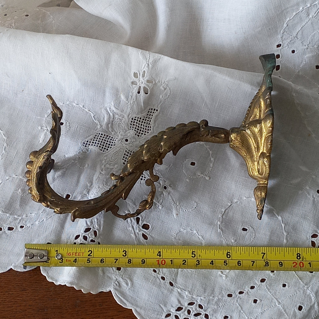 Decorative metal wall bracket with gold accents on a white lace background, measured with a tape measure.