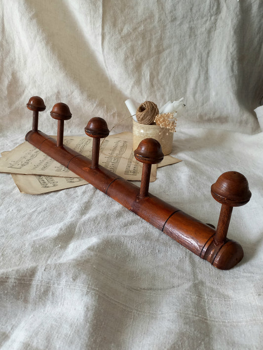 Wooden coat rack with five hooks on a textured white fabric background