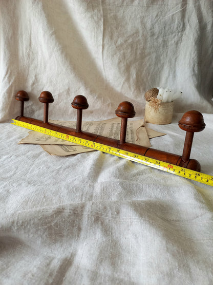 Wooden coat rack with five hooks on a textured white fabric background and a tape measure for reference.