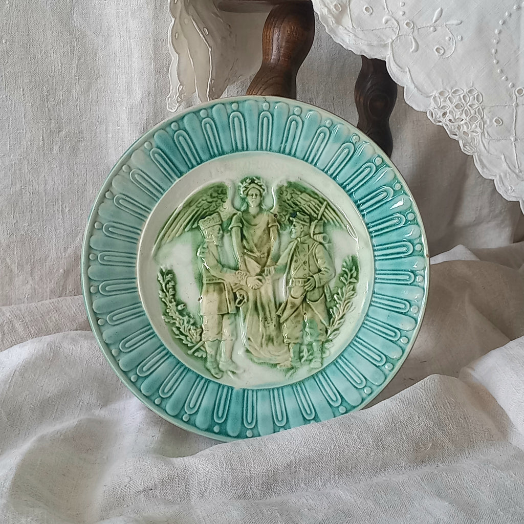 A French antique decorative majolica plate with stunning blue/green colours and an interesting historical background.

This lovely old plate was manufactured as a commemorative piece to celebrate the Franco-Russian Alliance made by the French Republic and the Russian Empire between 1891-1894 (military co-operation agreements) – and that lasted until 1917. The plate depicts a Russian and French soldier shaking hands with a winged female angel in between them.