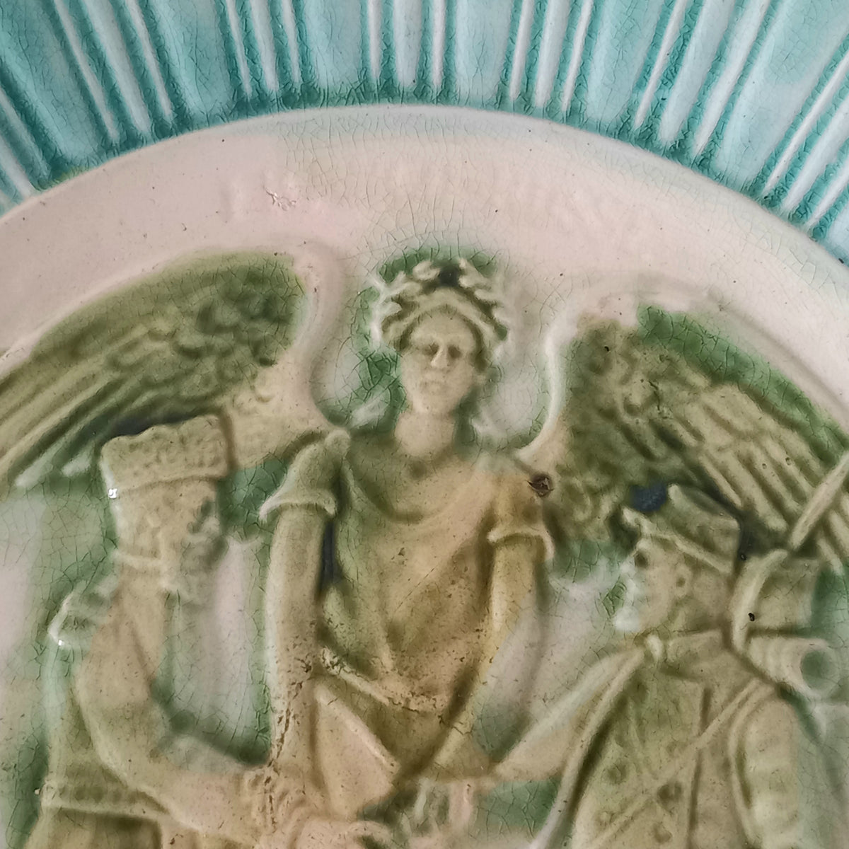 A French antique decorative majolica plate with stunning blue/green colours and an interesting historical background.

This lovely old plate was manufactured as a commemorative piece to celebrate the Franco-Russian Alliance made by the French Republic and the Russian Empire between 1891-1894 (military co-operation agreements) – and that lasted until 1917. The plate depicts a Russian and French soldier shaking hands with a winged female angel in between them.