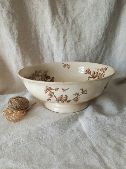 An off-white ceramic bowl with a brown floral and bird pattern, set against a draped linen fabric backdrop with a small ball of twine prop on the left.