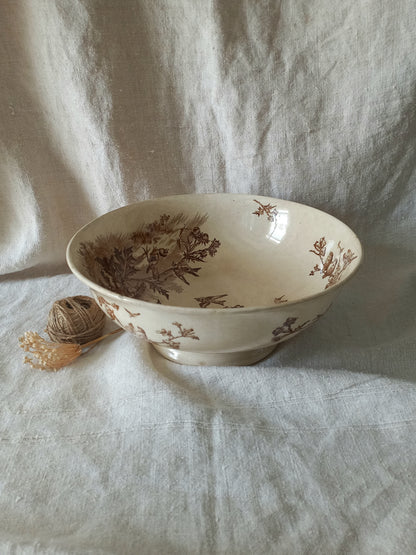 An off-white ceramic bowl with a brown floral and botanical pattern, styled on a draped white linen fabric background next to a small ball of twine.