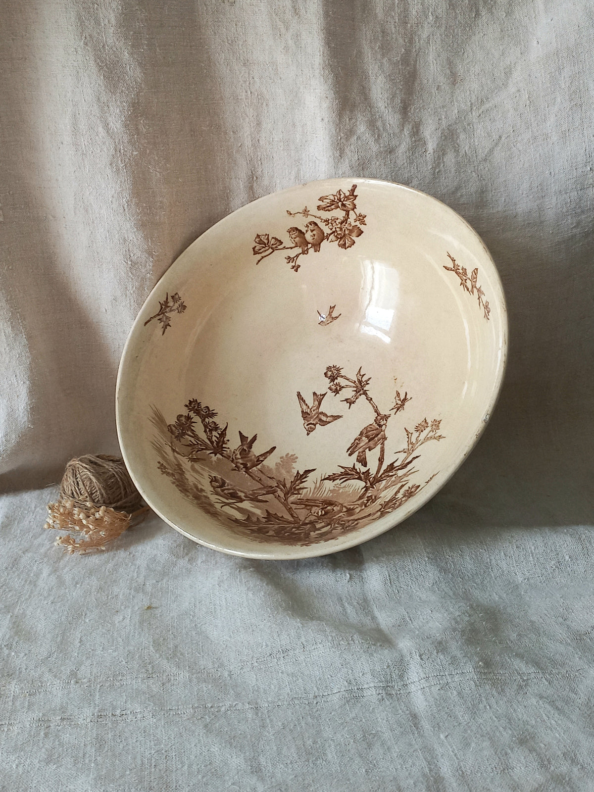 A cream-colored ceramic bowl with a brown sepia floral and bird pattern, resting on a textured light gray linen cloth.