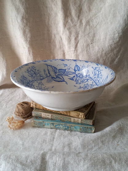 A white ceramic bowl with a blue floral pattern, displayed on a stack of vintage books next to a ball of twine on a draped linen fabric background.