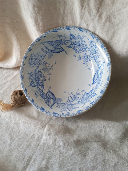 A round white ceramic bowl with a blue floral pattern, styled on a textured beige linen cloth next to a small ball of twine.