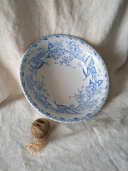 A white ceramic bowl with a blue floral pattern, styled on a textured beige linen fabric background next to a small ball of twine.