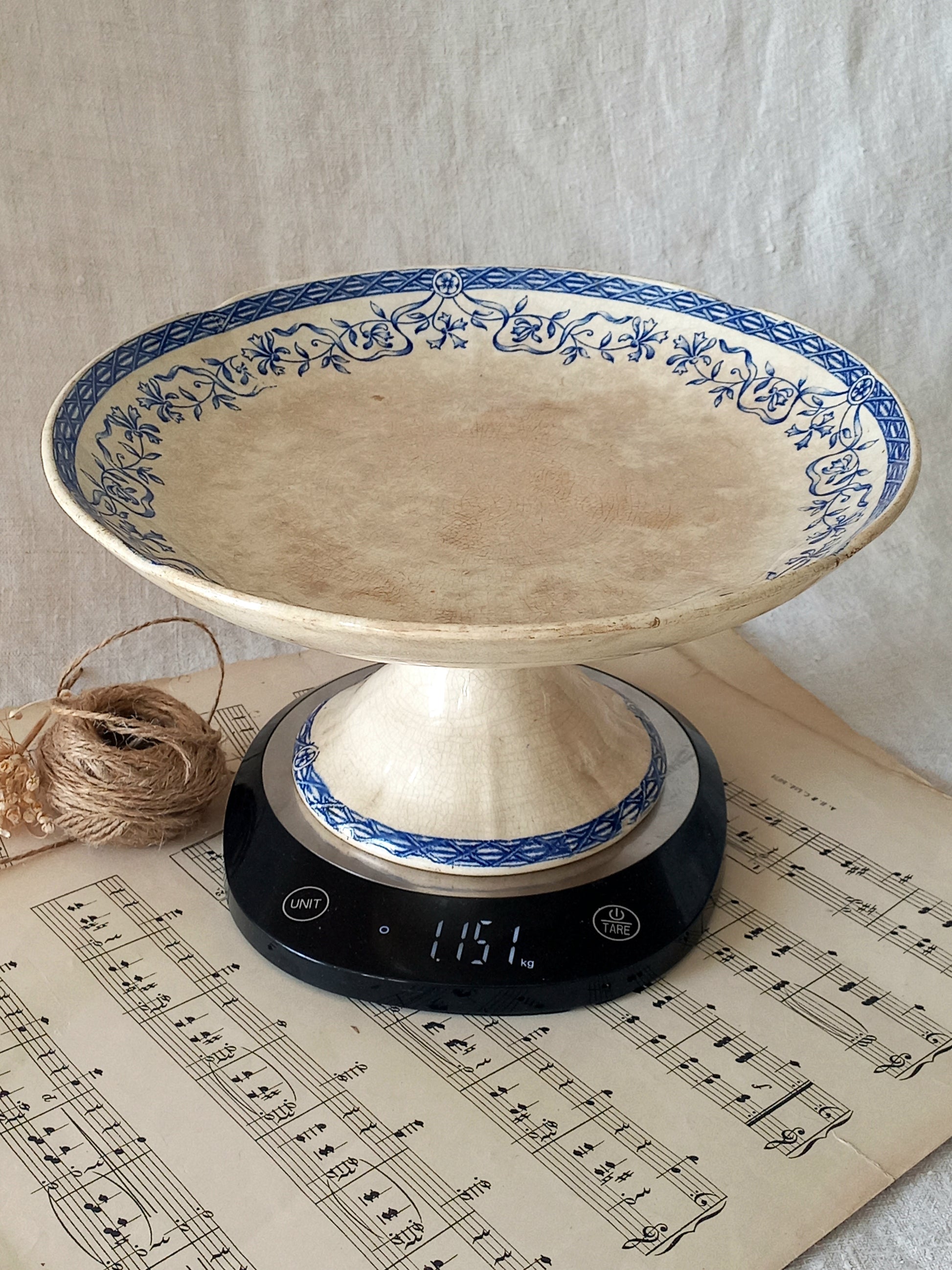 Decorative cake stand with blue floral patterns on a digital kitchen scale over sheet music.