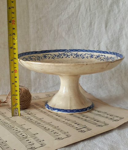 Decorative ceramic pedestal with blue floral patterns on a sheet of music, with a tape measure for scale.