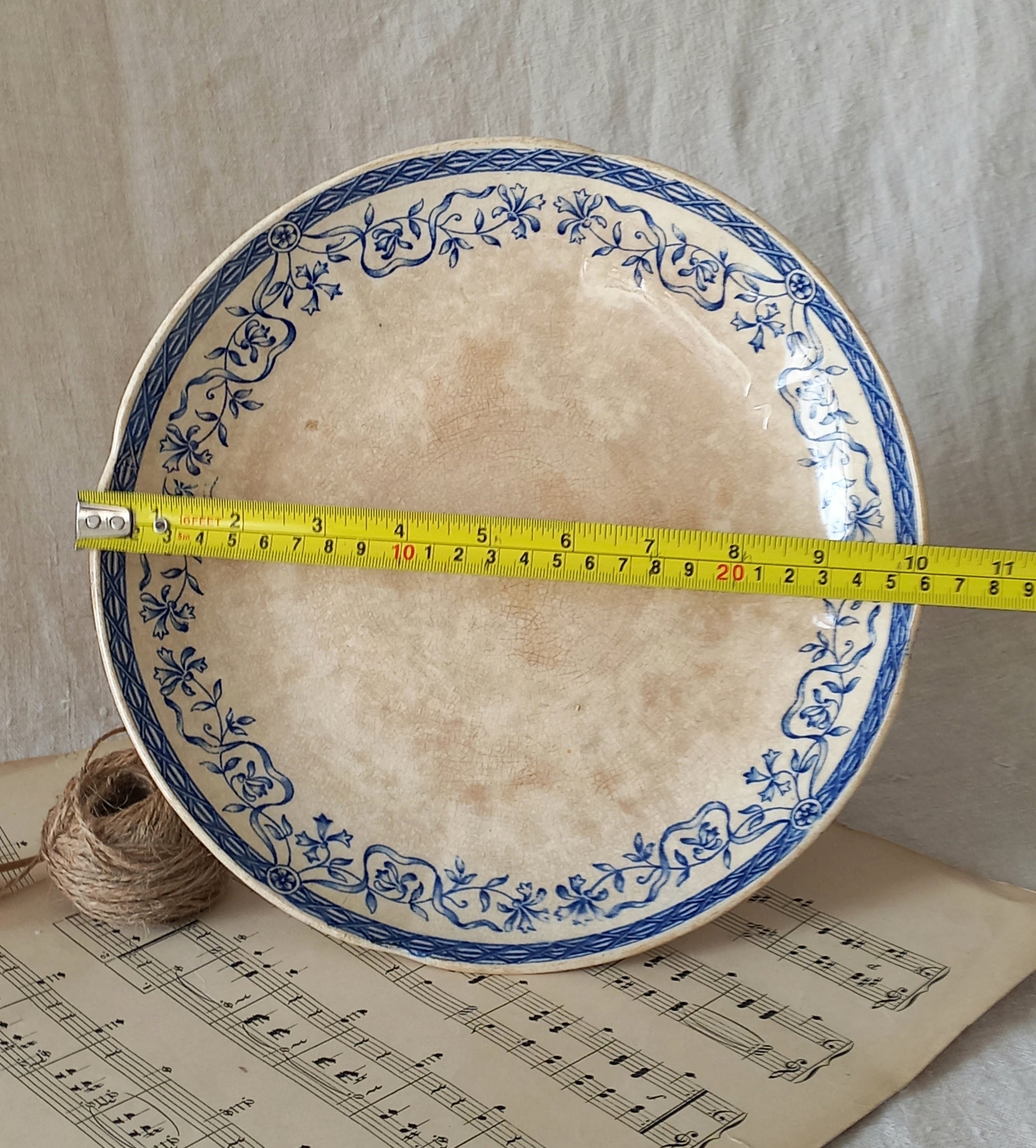 Decorative cake plate with blue floral patterns on a sheet of music, measured with a tape measure.