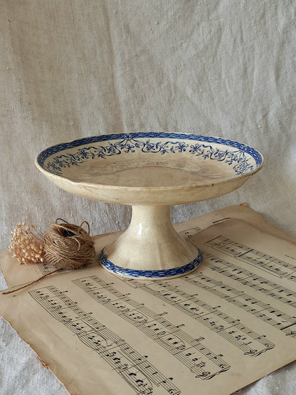 Decorative ceramic pedestal with blue floral patterns on a sheet of music, against a textured beige background.