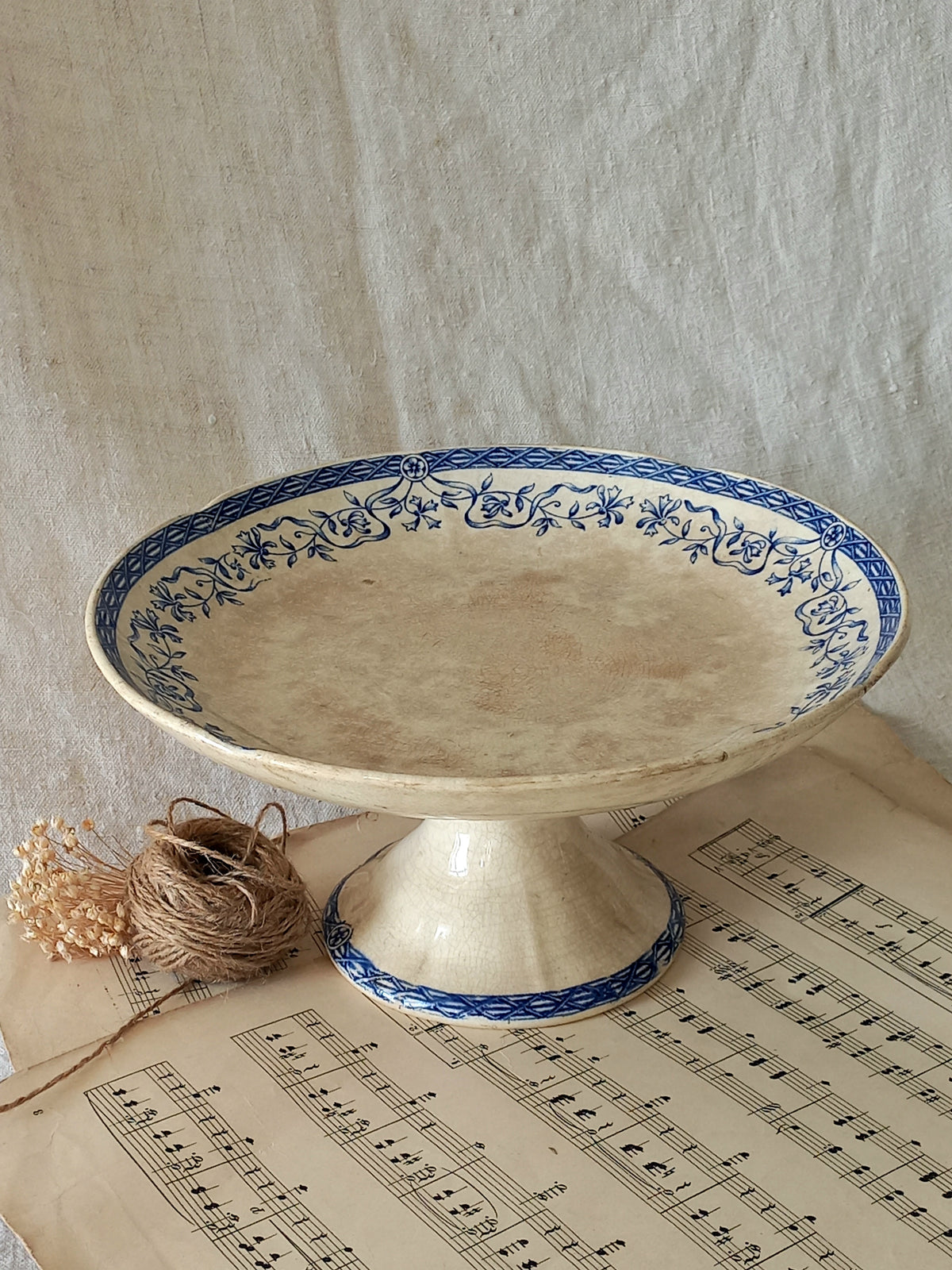 Decorative ceramic pedestal dish with blue floral patterns on a sheet of music.