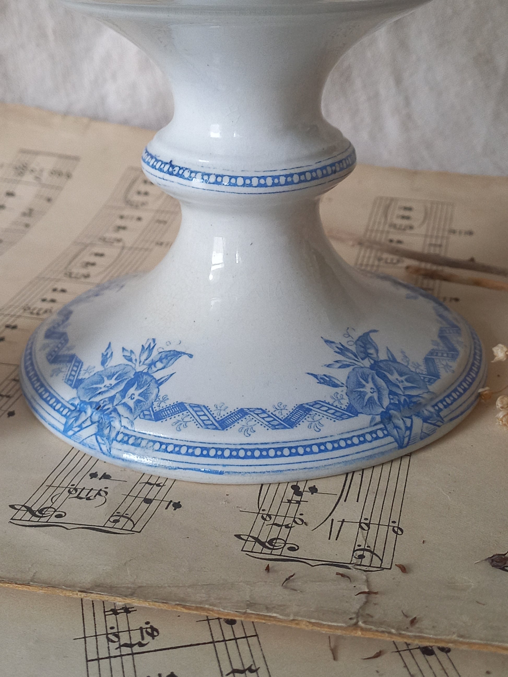 A white ceramic antique footed dish with blue floral and geometric patterns, resting on vintage sheet music.