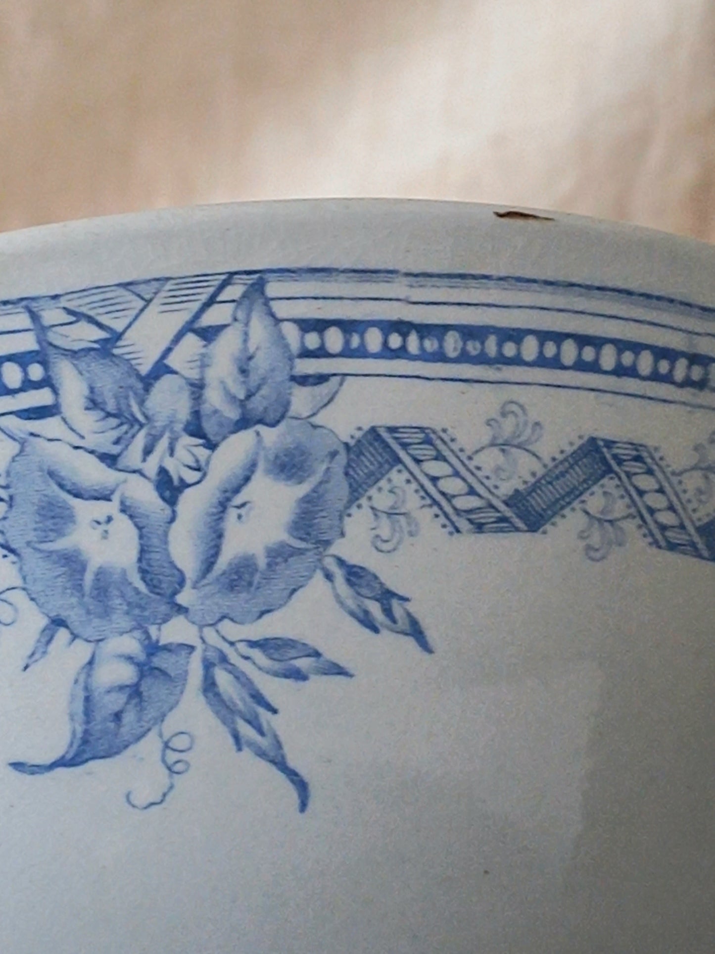 Close-up of a white ceramic surface with a blue floral and geometric pattern, showing part of a bowl or vase edge against a soft beige background.