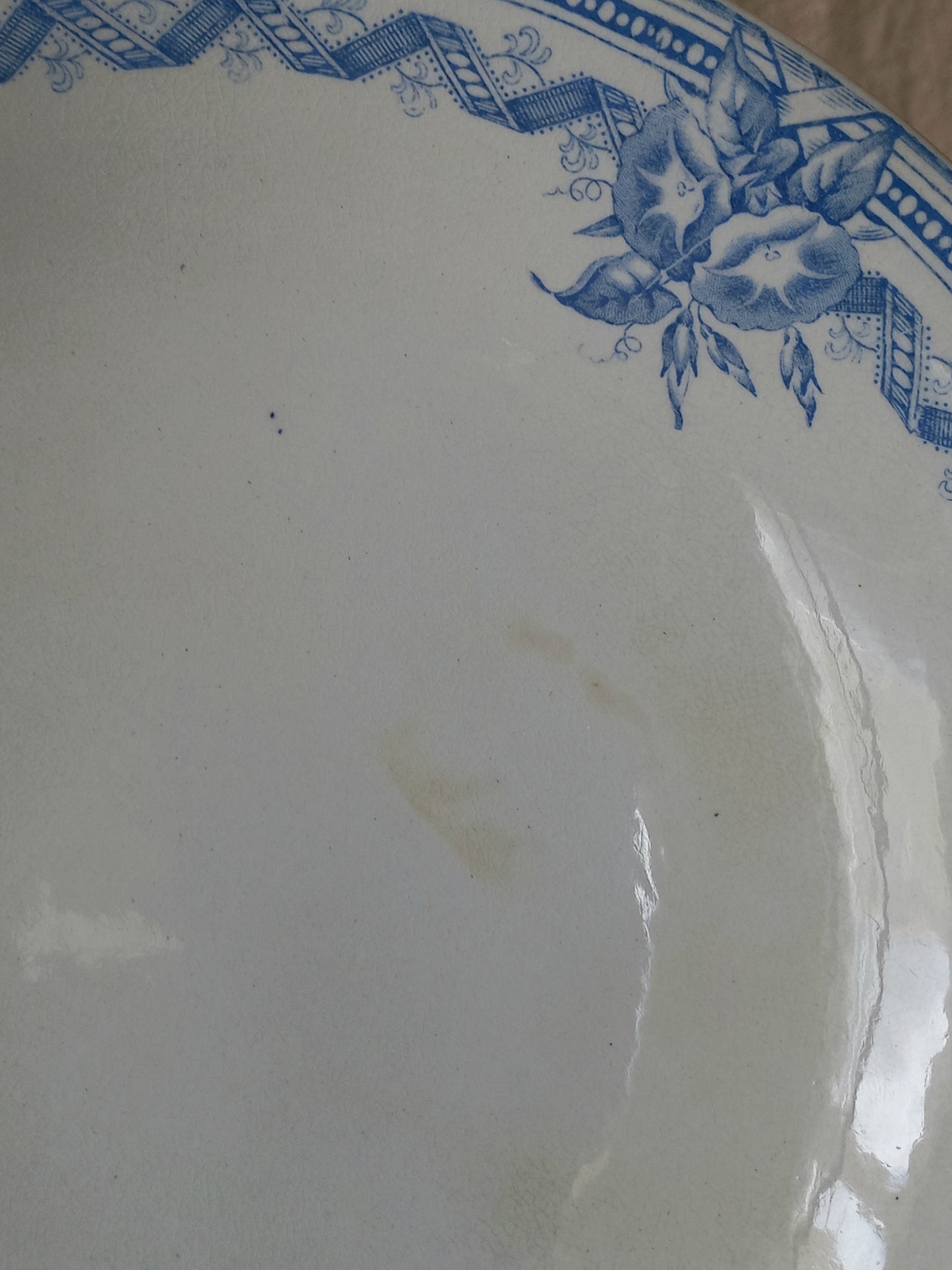 A close-up of a white ironstone footed bowl with a blue floral and geometric border design, showing a faint stain on the surface.