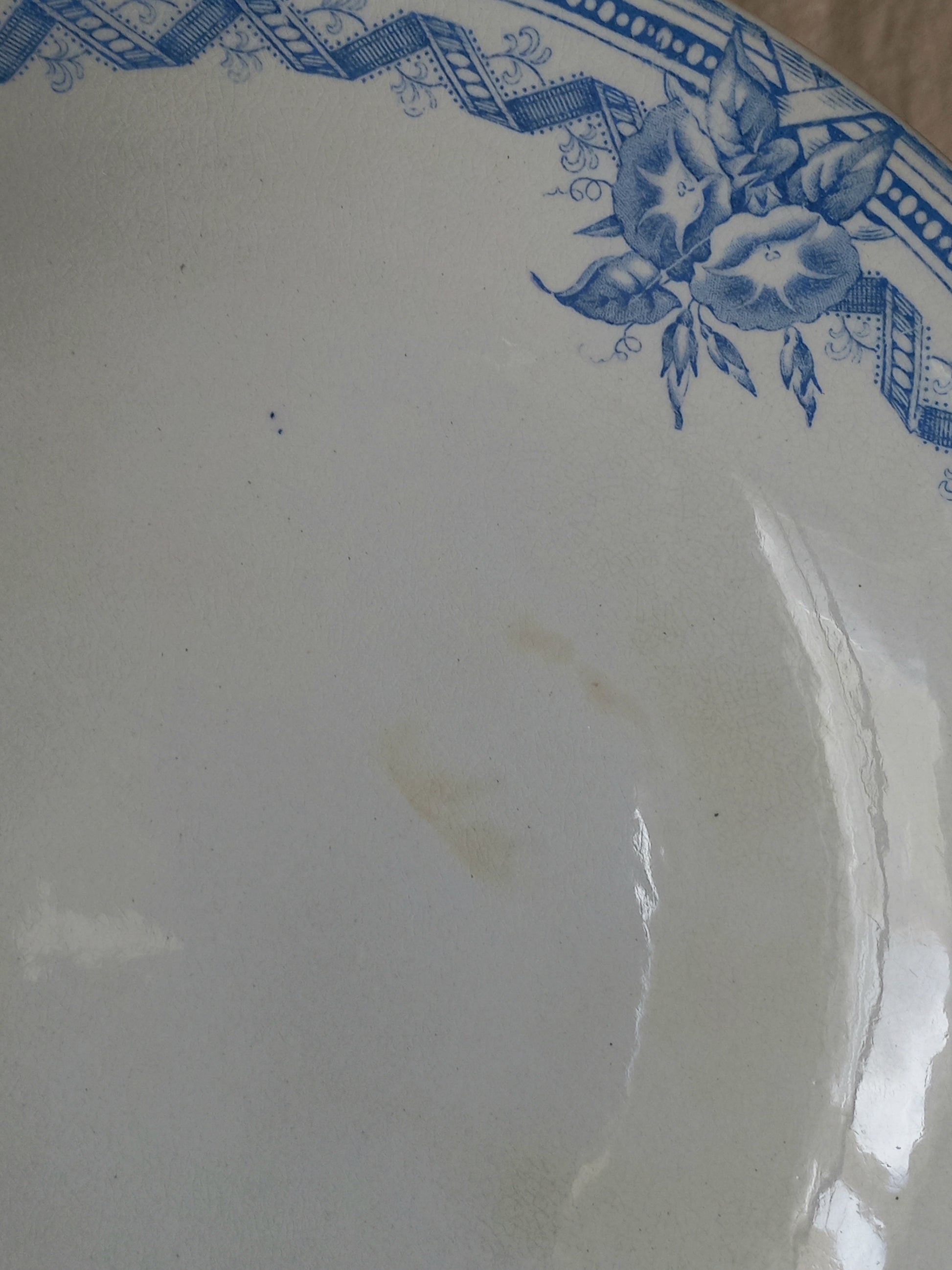 A close-up of a white ironstone footed bowl with a blue floral and geometric border design, showing a faint stain on the surface.