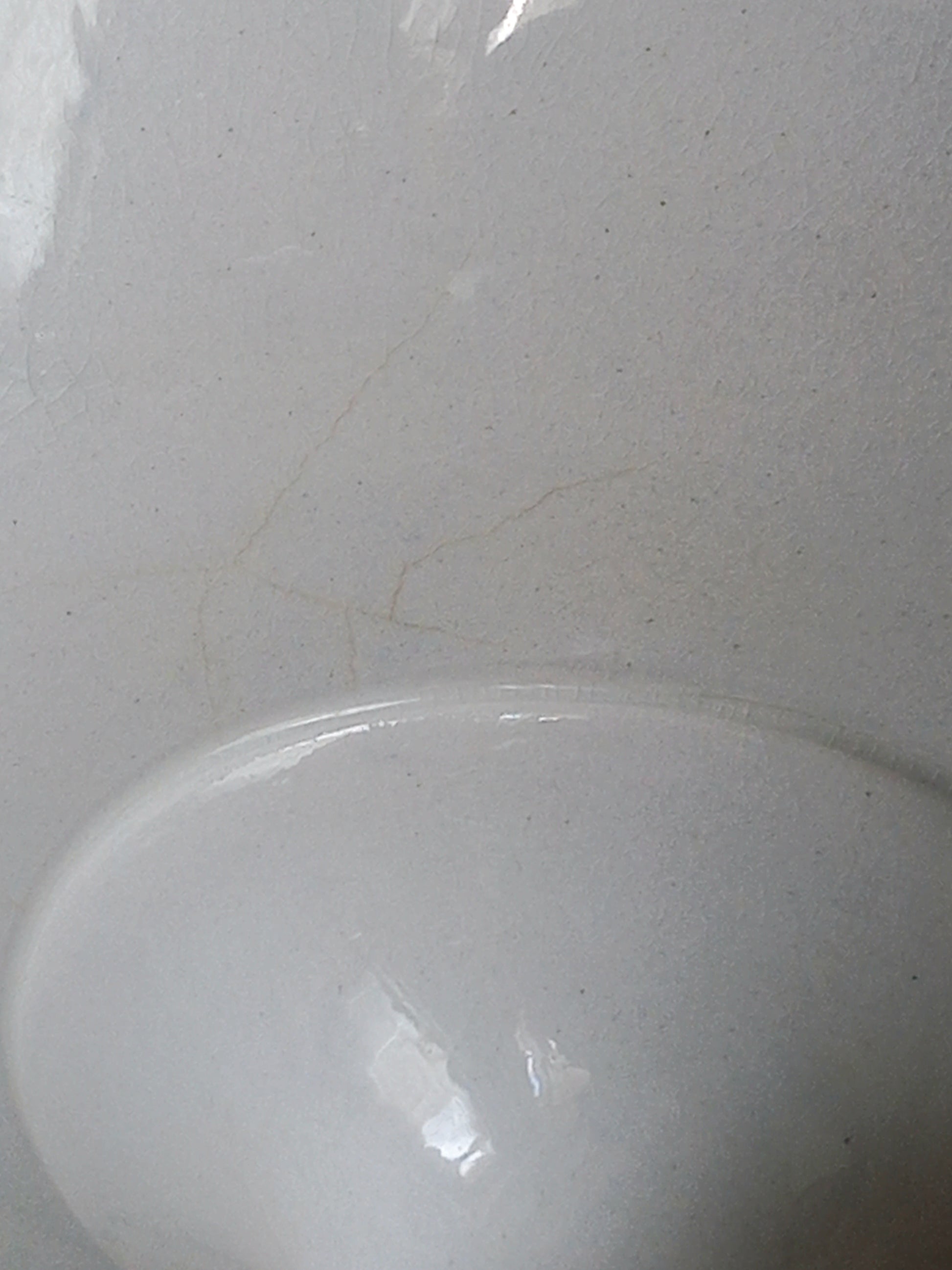 Close-up of an antique white ironstone footed bowl showing a minor spider hair on the surface.
