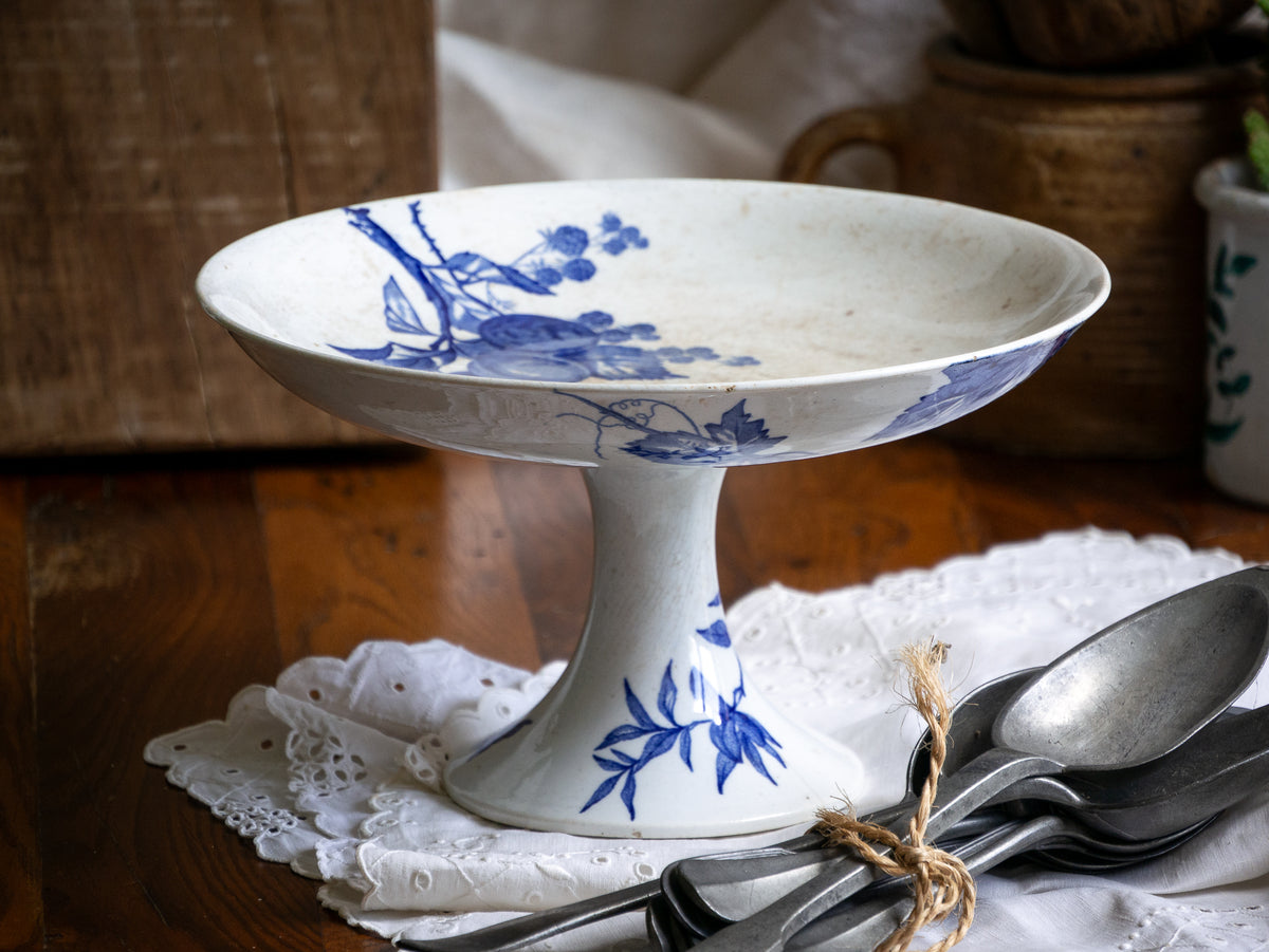 Compotier sur pied en faïence blanche ancienne française, orné d'un motif de libellule bleue et de fleurs. 