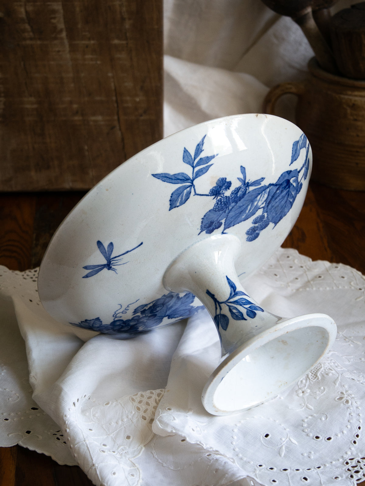 Compotier sur pied en faïence blanche ancienne française, orné d'un motif de libellule bleue et de fleurs. 