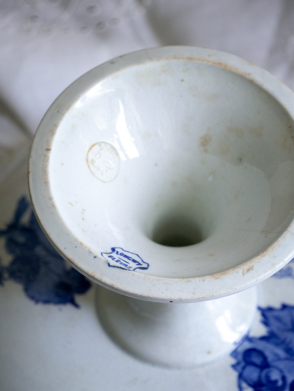 Compotier sur pied en faïence blanche ancienne française, orné d'un motif de libellule bleue et de fleurs. 