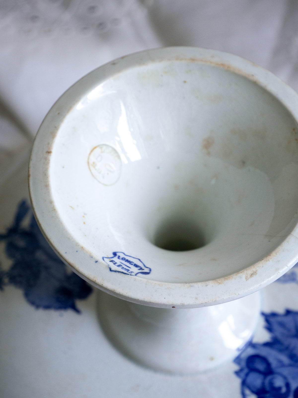 Compotier sur pied en faïence blanche ancienne française, orné d'un motif de libellule bleue et de fleurs. 